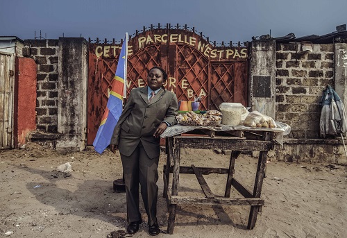 Une Grand Prêtre Mère accoudée à son étal dans la rue devant un portail (DR)